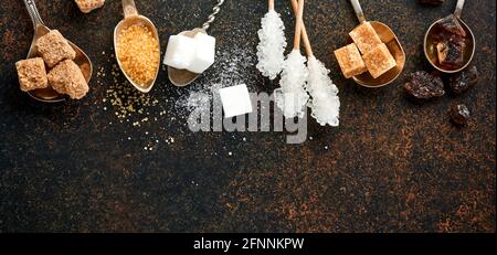 White sugar, cane sugar cubes, caramel in teaspoons on dark brown table concrete background. Assorted different types of sugar. Top view or flat lay. Stock Photo
