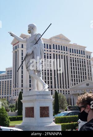 A young man wearing a face mask walking by a statue of Julius Caesar, wearing a gold face mask, at Caesars Palace in Las Vegas, Nevada. Stock Photo