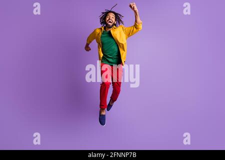 Full length photo of excited dark skin guy dressed yellow shirt jumping high running fast isolated purple color background