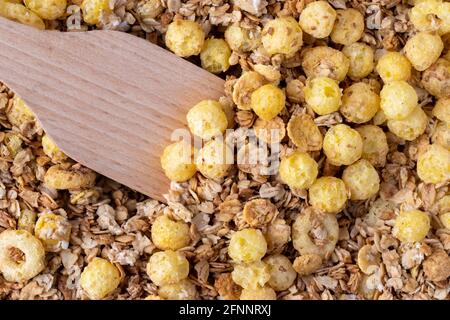 Organic homemade roasted crispy granola cereal with oatmeal and flaxseed flakes and crunchy corn balls and rings with wooden spatula or spoon. Top vie Stock Photo