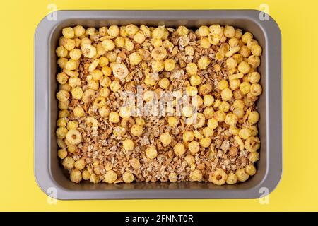 Organic homemade roasted crispy granola cereal with oatmeal and flaxseed flakes and crunchy corn balls and rings in baking tray on bright yellow backg Stock Photo