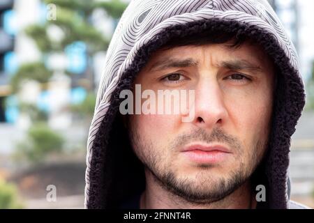 Serious handsome bearded man in a hood against a blurred background, closeup portrait Stock Photo