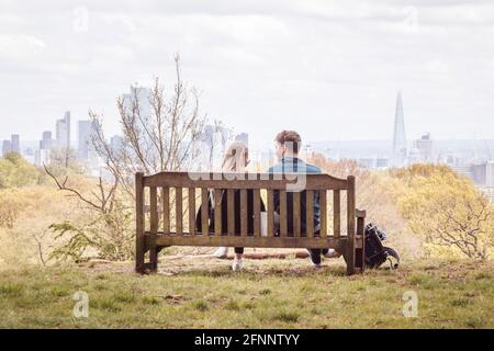 A couple (male and female) sitting on a bench on Hampstead Heath overlooking the City of London during the coronavirus pandemic, UK Stock Photo
