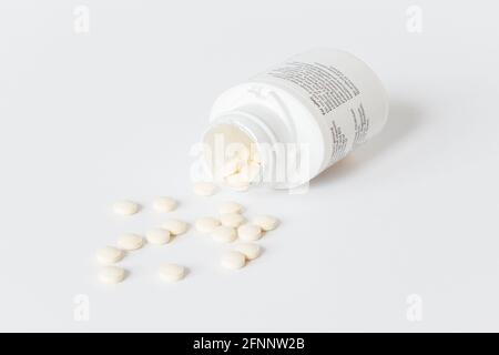 Vitamin tablets spilling out of an open plastic container on a white background Stock Photo