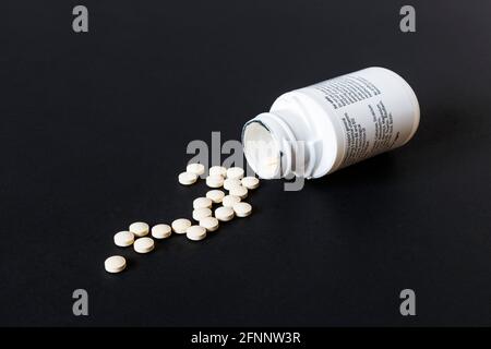 Vitamin tablets spilling out of an open white plastic container on a black background Stock Photo