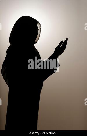 Silhouette of Muslim woman in a veil sitting and praying with the night ...