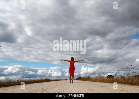 Woman walking alone on straight country road.  Cloudy sky.   France. Stock Photo