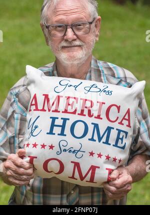 Elderly man holds a patriotic God Bless America pillow in honor of American Independence Day.. Stock Photo