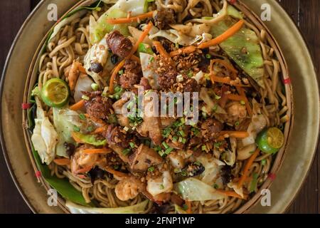 Filipino hand-pulled pancit noodles on a bilao with vegetable stir-fry, garlic longganiza, crispy bagnet, and calamans Stock Photo