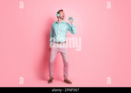 Full body photo of attractive happy funky man hold phone sing wear headphones isolated on pastel pink color background Stock Photo