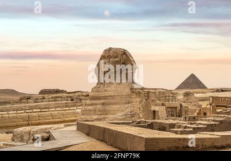 Egyptian Great Sphinx full body portrait with head, feet with all pyramids of Menkaure, Khafre, Khufu in background on a clear, blue sky day in Giza, Stock Photo