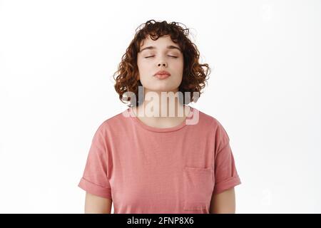 Romantic beautiful young woman close eyes, waiting for kiss with puckered lips, daydreaming about kissing someone, standing against white background Stock Photo