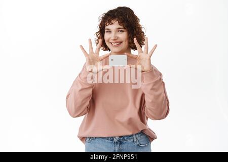 Bank and finance concept. Beautiful girl holds and shows credit card, smiles happy, making announcement of new banking feature, shopping online Stock Photo