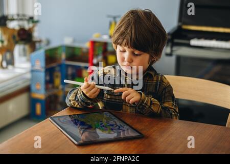 Innocent boy using digitized pen to draw on graphic tablet. Kid using digital tablet and stylus pen at home. Stock Photo