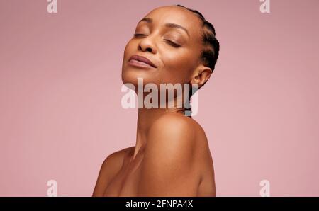 Close-up of a pretty female model with healthy skin on pink background. Woman having flawless skin and eyes closed. Stock Photo