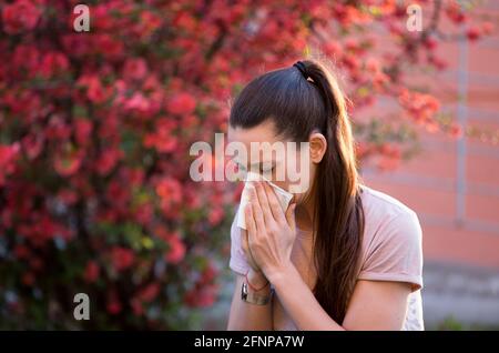 Young pretty woman sneezing in front of blooming tree. Spring allergy concept Stock Photo