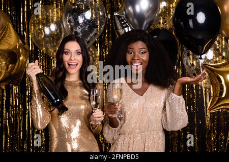 Photo of tow amazed festive ladies hold glasses champagne bottle party isolated on shine glitter bright background Stock Photo