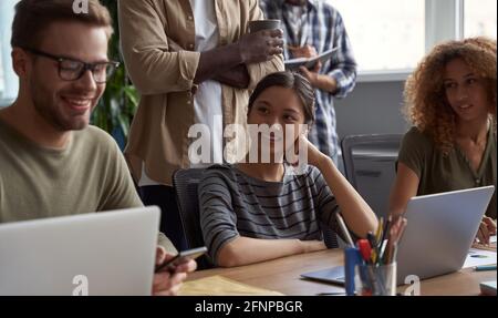 Young multiracial business people at work. Happy beautiful asian woman smiling while communicating with colleagues, enjoying working together in the Stock Photo