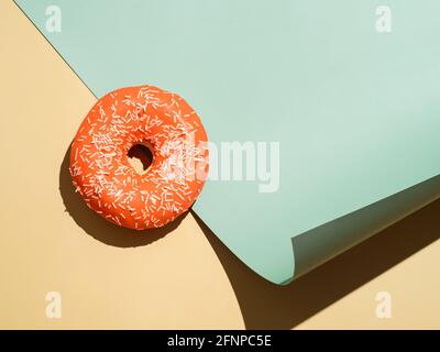 Creative layout made with delicious glazed donut.Flat lay orange glazed donut or doughnut on pastel cream beige and soft green colors neutral background. Bright sun light with hard shadows, copy space Stock Photo