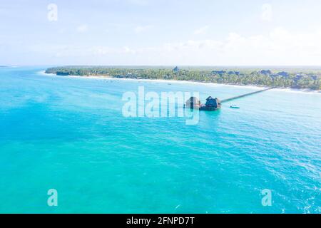 Aerial shot of the Stilt hut with palm thatch roof washed with turquoise Indian ocean waves on the white sand sandbank beach on Zanzibar island, Tanza