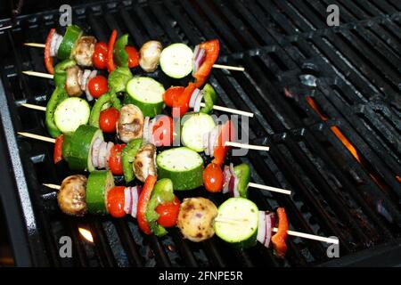 Close-up of vegetable skewers, with mushroom, onions, green pepper, red pepper, cherry tomatoes, Zucchini, and seasoning, on a barbecue grill. Stock Photo