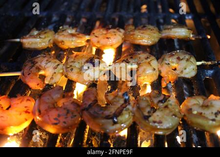 Close-up of glazed and seasoned shrimp on skewers being grilled on a barbecue. Stock Photo