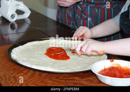 Close-up of woman and small child making homemade pizza. Hands only in frame. Stock Photo