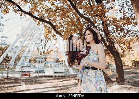 Two young women in vintage dresses having fun in park near ferris wheel