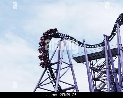 Russia, Sochi 16.04.2021. Fragment of extreme attraction roller coaster with people riding on it high against blue cloudy sky Stock Photo