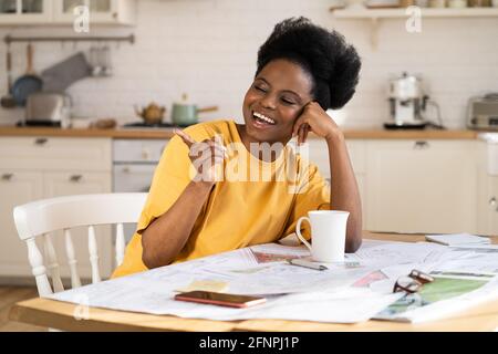 Overjoyed black businesswoman laugh work from home. Cheerful architect sit at table with blueprints Stock Photo