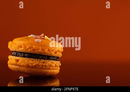 Delicious orange macarons with chocolate ganache filling. Isolated french delicious cookies. Shot on Dark orange background with reflections and copy Stock Photo