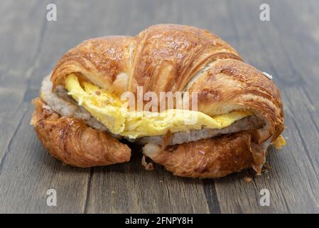 Delicious croissant sandwich loaded with scrambled eggs, melted cheese, and sausage patty for a complete meal. Stock Photo