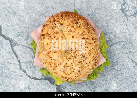 Overhead view of everything bagel bun envelops this non traditional ham sandwich loaded with lettuce, meat slices, and onion. Stock Photo