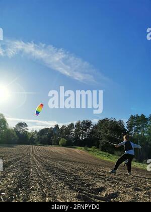 A happy boy launches a bright rainbow kite into the sky in a plowed field Stock Photo