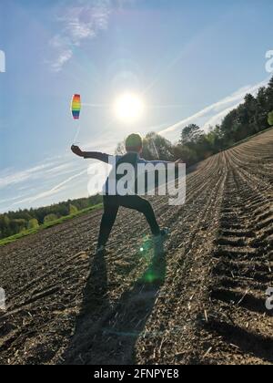 A happy boy launches a bright rainbow kite into the sky in a plowed field Stock Photo