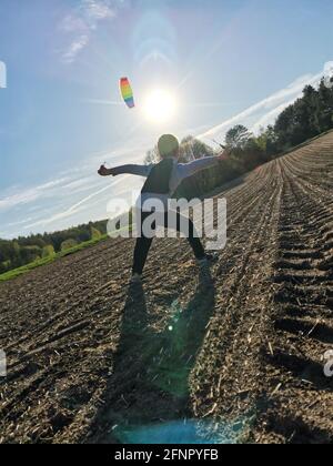 A happy boy launches a bright rainbow kite into the sky in a plowed field Stock Photo