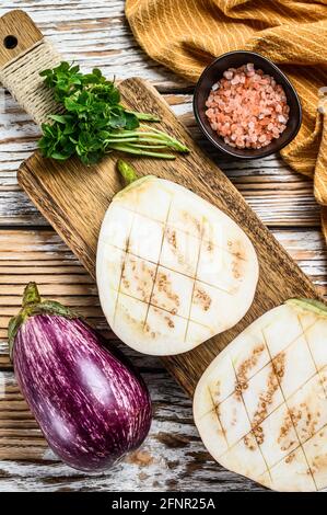 Sliced raw purple Aubergine or eggplant. White wooden background. Top view Stock Photo