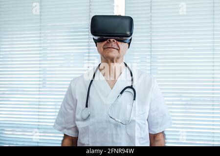 Doctor at the window of a hospital, using virtual reality glasses for medical purposes, looking up Stock Photo