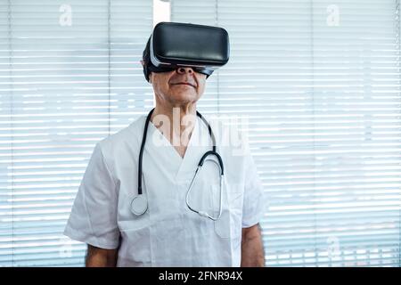 Doctor at the window of a hospital, using virtual reality glasses for medical purposes, looking to the right Stock Photo