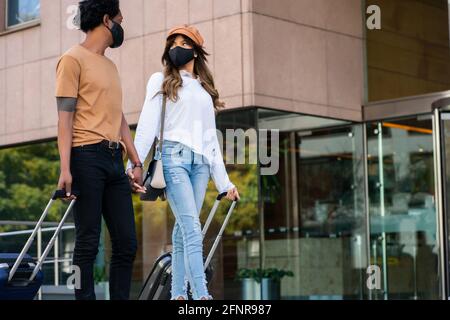 Tourist couple carrying suitcase while walking outdoors. Stock Photo