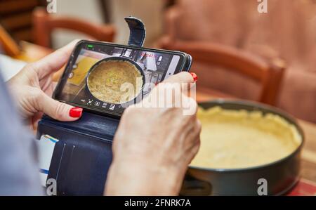 Woman shoots video on mobile phone mold for making cheese cake, step-by-step recipe from the Internet. Stock Photo