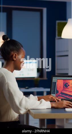 Dark skin gamer developer working at video game in midnight from business office using professional laptop. African player testing online video games on pc with modern technology network wireless. Stock Photo