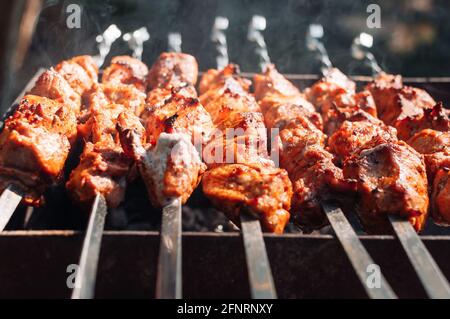 Cooking marinated pork skewers on the grill. Juicy pieces of meat in the marinade are covered with smoke from the fire. Fried pork kebab on an open Stock Photo