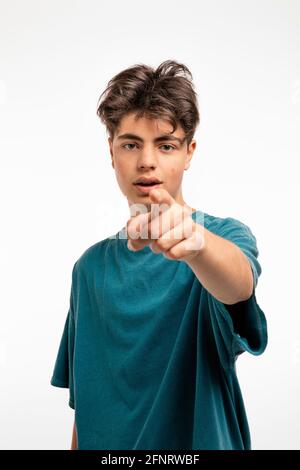 Portrait of teenager on white background in studio. The boy is standing and pointing with his finger at you who are standing in front of him Stock Photo