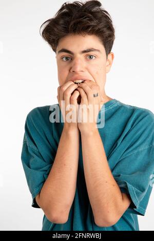 Portrait of young boy distressed and full of fear, scared. He is standing on white background with his fingers in his mouth Stock Photo