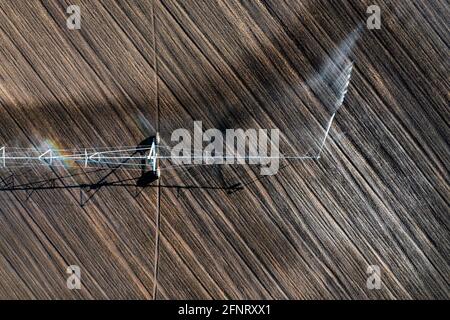 A field irrigation sprinkler system waters rows of fields crops on farmland. Center Pivot Irrigation System Stock Photo