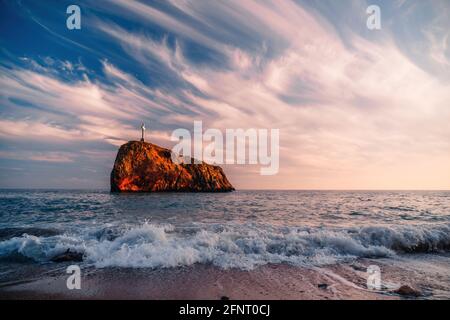 Bright sea sunset. The waves crash into the rock, lit by the warm sunset, sand and pebbles, volcanic basalt as in Iceland. Sea wave breaks into Stock Photo