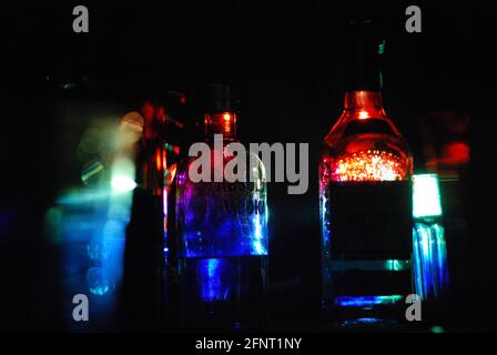 Close up of a few backlit bottles of alcohol (including Absolut vodka) with dramatic colors of red and blue on a black background. Stock Photo