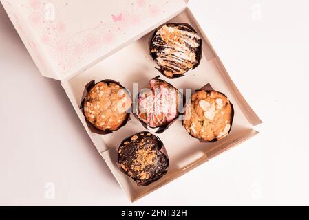closeup of colorful muffins and cupcakes box isolated on white background. muffins with chocolate and sugar glaze and icing, concept of sugar consumpt Stock Photo