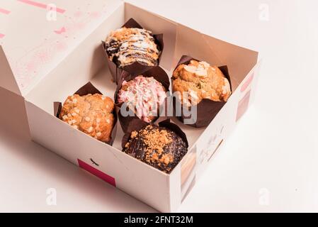 closeup of colorful muffins and cupcakes box isolated on white background. muffins with chocolate and sugar glaze and icing, concept of sugar consumpt Stock Photo
